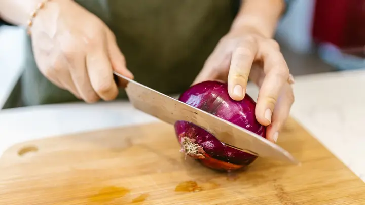 Mãos cortando uma cebola roxa na tábua