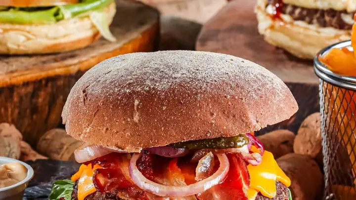Hambúrgueres artesanais com bacon, queijo e cebola roxa sobre tábuas de madeira