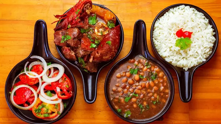 Panelinhas de ferro com carne ao molho, feijão, arroz e vinagrete sobre mesa de madeira